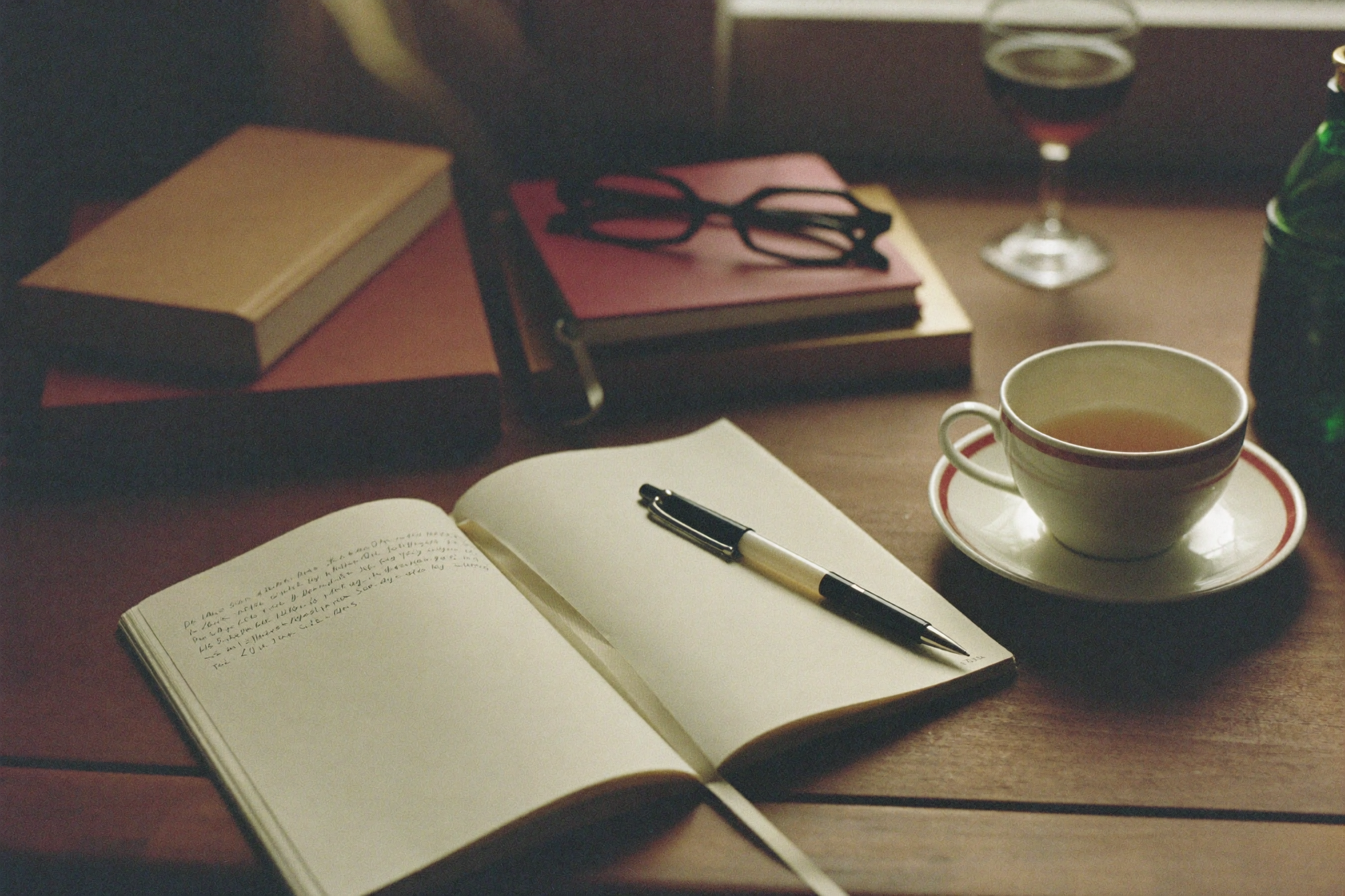 Un carnet ouvert, des livres et une tasse de thé dans une lumière chaude, évoquant la réflexion et la recherche.